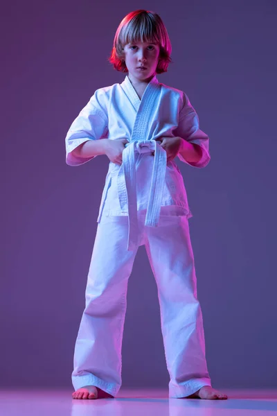 Niño serio, niño pequeño, taekwondo o atletas de karate en doboks posando aislados sobre fondo de color muy peri en neón. Concepto de deporte, artes marciales — Foto de Stock