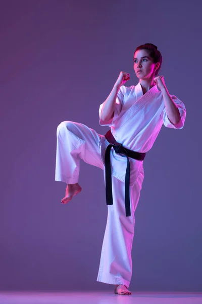 Portret van vrouwelijke taekwondo, karate atleten in doboks doen basisbewegingen geïsoleerd op paarse achtergrond in neon. Begrip sport, vechtsport — Stockfoto