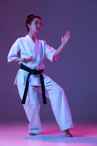 Portret van vrouwelijke taekwondo, karate atleten in doboks doen basisbewegingen geïsoleerd op paarse achtergrond in neon. Begrip sport, vechtsport — Stockfoto