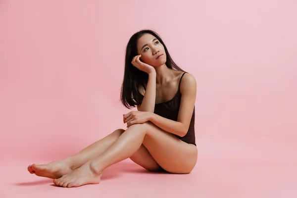 Retrato de estudio de mujer tierna de aspecto soñador sentada y posando en traje aislado sobre fondo rosa —  Fotos de Stock