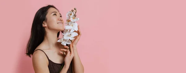Mulher jovem macia em bodysuit marrom com flor de orquídea branca macia posando isolado sobre fundo de estúdio rosa. Folheto — Fotografia de Stock