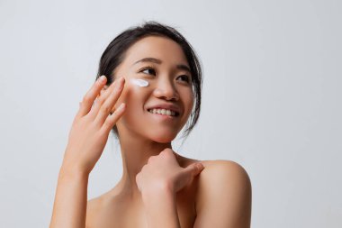 Cilt bakımında gülümseyen genç bir kadının özel krem sürerek nemlendirici yüzü.