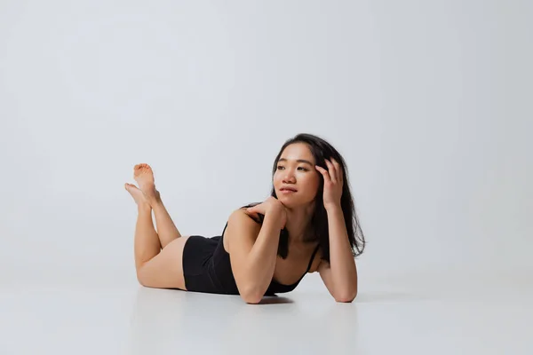 Retrato de hermosa mujer asiática en traje negro tumbado en el suelo, posando aislado sobre fondo gris estudio —  Fotos de Stock