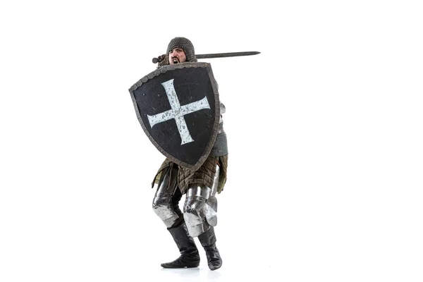 Portrait of brutal serious man, medieval warrior or knight in protective covering with sword preparing to attack isolated over white studio background — Stock Photo, Image