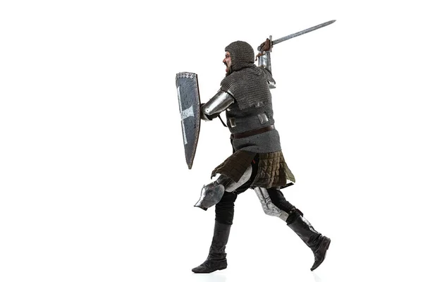 Retrato del hombre concentrado, guerrero medieval en armadura de cadena con espada y escudo atacando al enemigo aislado sobre fondo blanco del estudio —  Fotos de Stock