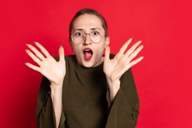 Şok olmuş, şaşırmış, kısa saçlı, koyu renk kazaklı bir öğrenci kırmızı arka planda ağzı açık duruyor. Duyguların kavramı, çalışma, reklam