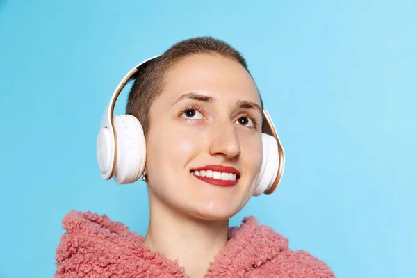 Chica bonita feliz, estudiante con pelo corto con capucha rosa en auriculares aislados sobre fondo azul. Concepto de emociones, música — Foto de Stock