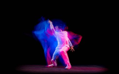 Erkek hip-hop dansçısının dinamik portresi. Karmaşık neon ışıkta koyu arka planda izole edilmiş. Gençlik kültürü, hip-hop, hareket, tarz ve moda, aksiyon.