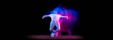 Erkek hip-hop dansçısının dinamik portresi. Karmaşık neon ışıkta koyu arka planda izole edilmiş. Gençlik kültürü, hip-hop, hareket, tarz ve moda, aksiyon.