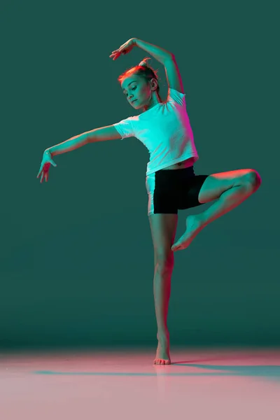 Tańczę. Mała elastyczna dziewczyna, gimnastyka rytmiczna trening artysty odizolowany na zielonym tle studio w neonowym różowym świetle. Grace w ruchu, akcja. Wykonywanie ćwiczeń w zakresie elastyczności. — Zdjęcie stockowe