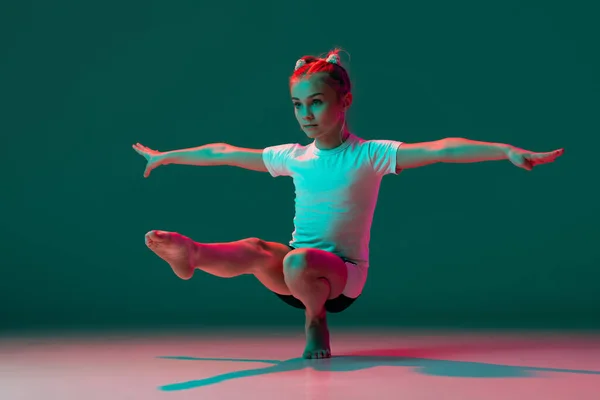 총알받이 야. 유연 한 작은 소녀, 리듬 체조 예술가가 네온 핑크 빛의 녹색 스튜디오 배경에서 고립되어 훈련받고 있습니다. 그 레이스가 움직이고, 행동 합니다. 융통성 있게 운동을 함. — 스톡 사진