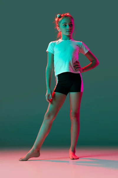 Portret pięknej dziewczynki, artystki gimnastyki rytmicznej w mundurze sportowym, pozującej na zielonym tle studia w neonowym, różowym świetle. Sport, dzieciństwo, koncepcja studiów — Zdjęcie stockowe