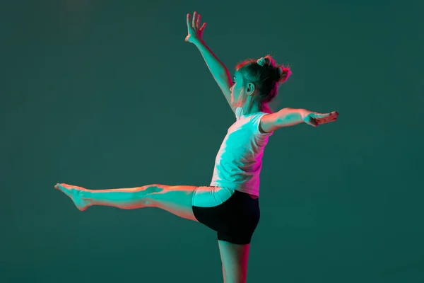 Malá ohebná dívka, rytmické gymnastika výtvarník školení izolované na zeleném pozadí studia v neonově růžové světlo. Grace v pohybu, akce. Cvičení v pružnosti. — Stock fotografie