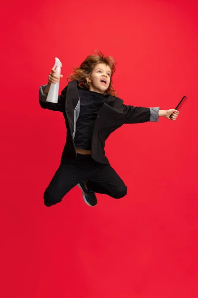 Full längd porträtt av Liitle pojke, unge i bild av snygg frisör, frisör hoppa isolerad på röd bakgrund. Begreppet yrke, moderna specialister, barndom — Stockfoto