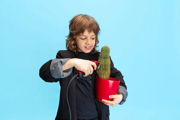 Kaktusz szeletelés. Képregény portré a kisfiú, gyerek hatalmas fekete kabát, mint a borbély szórakozás elszigetelt kék háttér. — Stock Fotó