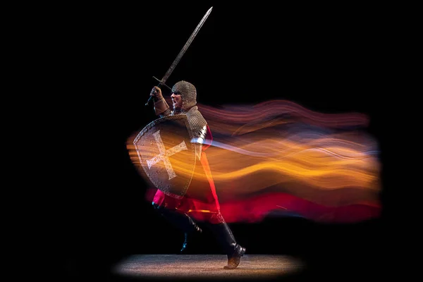 Ogniste pióra. Portret brutalnego poważnego mężczyzny, średniowiecznego rycerza lub wojownika w zbroi i łańcuszku walczącego na ciemnym tle w neonowym świetle mieszanym. Sztuka, historia, kreatywność — Zdjęcie stockowe