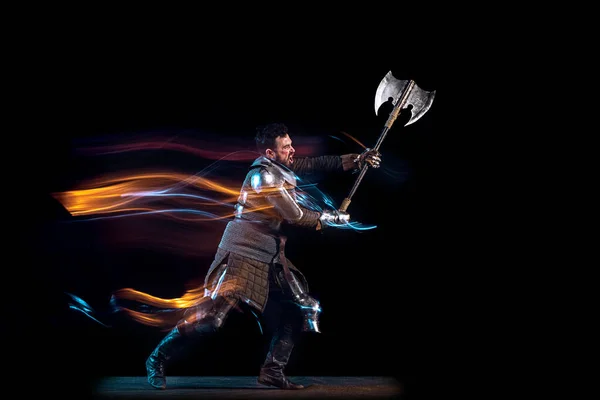 Retrato dinâmico de homem sério brutal, cavaleiro medieval com machado balançando lutando isolado sobre fundo escuro em néon luz mista. Arte, história, criatividade — Fotografia de Stock