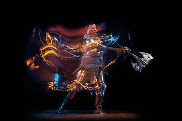 Retrato dinâmico de homem sério brutal, cavaleiro medieval com machado balançando lutando isolado sobre fundo escuro em néon luz mista. Arte, história, criatividade — Fotografia de Stock