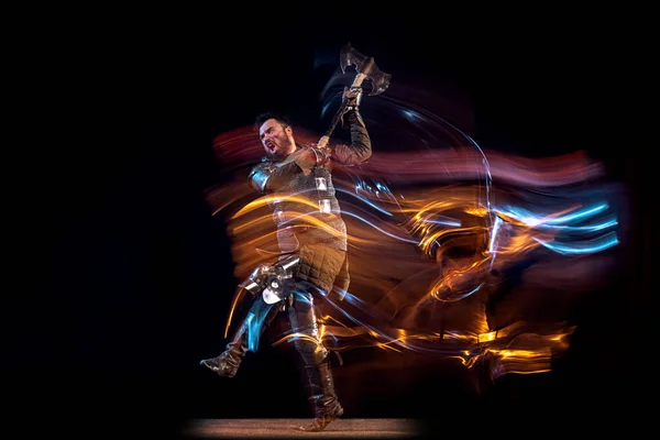 Retrato dinámico del hombre serio brutal, caballero medieval con el hacha oscilante que lucha aislado sobre fondo oscuro en luz mezclada de neón. Arte, historia, creatividad — Foto de Stock