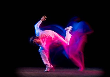 Erkek hip-hop dansçısının dinamik portresi. Karmaşık neon ışıkta koyu arka planda izole edilmiş. Gençlik kültürü, hip-hop, hareket, tarz ve moda, aksiyon.