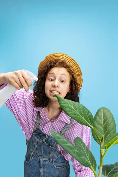 Portrait of young pretty girl, female gardener in work uniform watering flower isolated on white background. Concept of job, emotions, agronomy — Stock Photo, Image