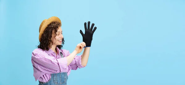 Flyer dengan gadis muda yang bahagia, tukang kebun dalam seragam kerja dan topi menempatkan sarung tangan di terisolasi di latar belakang biru. Konsep pekerjaan, emosi, agronomi, eko — Stok Foto