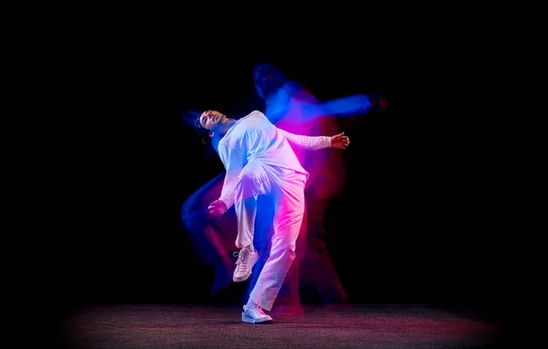 Dynamický portrét mužské hip-hopové tanečnice tančící izolovaně na tmavém pozadí ve smíšeném neonovém světle. Mládež kultura, hip-hop, pohyb, styl a móda, akce. — Stock fotografie