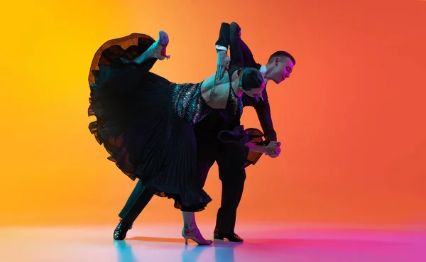 Dynamisch portret van jonge mooie man en vrouw dansen ballroom dans geïsoleerd over gradiënt oranje roze achtergrond in neon licht. Schoonheid, kunst, sport concept — Stockfoto