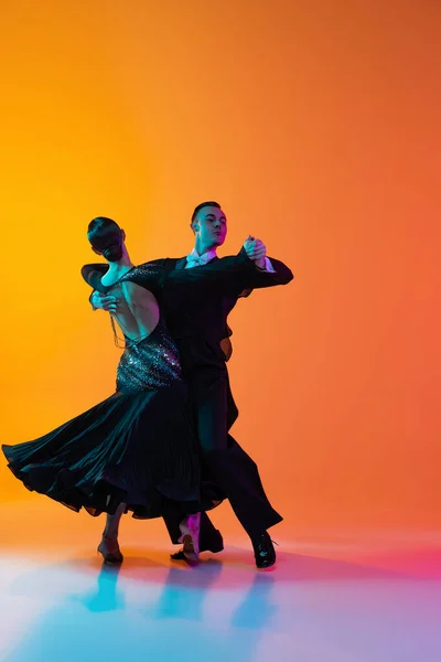 Pełnowymiarowy portret młodego pięknego mężczyzny i kobiety tańczącego taniec towarzyski odizolowany od gradientowego pomarańczowego różowego tła w neonowym świetle. Piękno, sztuka, koncepcja sportu — Zdjęcie stockowe