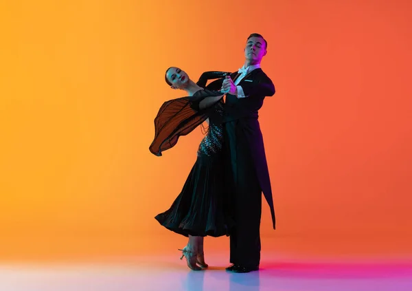 Retrato de un joven hermoso hombre y una mujer bailando bailes de salón aislados sobre un fondo rosa anaranjado degradado en luz de neón. Belleza, arte, concepto deportivo —  Fotos de Stock