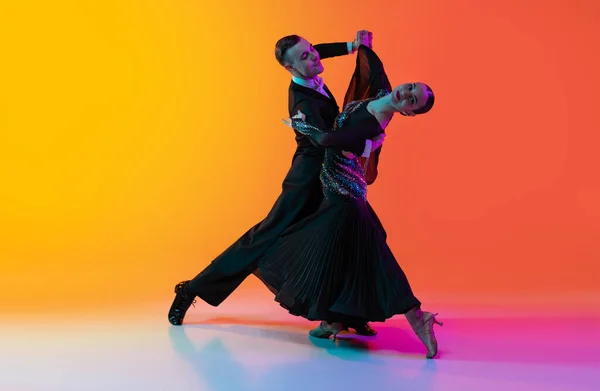 Retrato completo de jovem e belo homem e mulher dançando dança de salão isolado sobre gradiente laranja fundo rosa em luz de néon. Beleza, arte, conceito de esporte — Fotografia de Stock