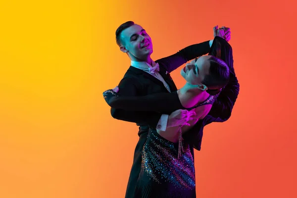 Retrato dinâmico do jovem belo homem e mulher dançando dança de salão isolado sobre gradiente laranja fundo rosa em luz de néon. Beleza, arte, conceito de esporte — Fotografia de Stock