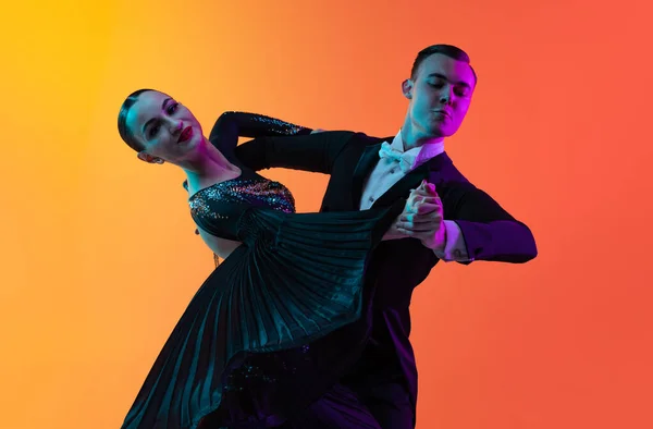 Zbliżenie emocjonalnie tańcząca para, piękny mężczyzna i kobieta tańczący walca odizolowany na gradientowym pomarańczowym tle w neonowym świetle. Piękno, sztuka, koncepcja sportu — Zdjęcie stockowe