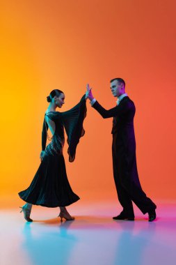 Genç ve güzel bir adamın dinamik portresi dans eden balo salonu dansı gradyan turuncu pembe arka planda neon ışıklarıyla izole edilmiş. Güzellik, sanat, spor konsepti