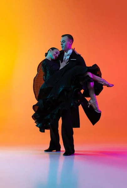 Retrato completo de jovem e belo homem e mulher dançando dança de salão isolado sobre gradiente laranja fundo rosa em luz de néon. Beleza, arte, conceito de esporte — Fotografia de Stock