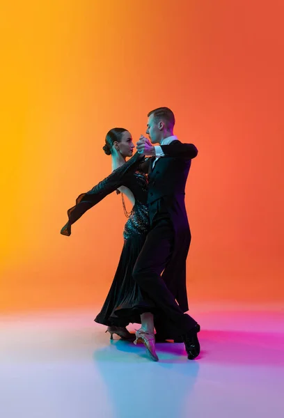 Retrato completo de jovem e belo homem e mulher dançando dança de salão isolado sobre gradiente laranja fundo rosa em luz de néon. Beleza, arte, conceito de esporte — Fotografia de Stock