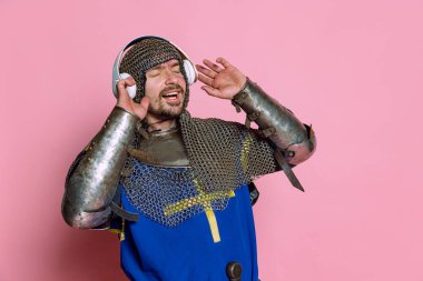 Orta çağ savaşçısı, orta çağ savaşçısı ya da kulaklıkla müzik dinleyen pembe arka planda izole edilmiş hoş bir yüz ifadesi olan bir adam portresi.