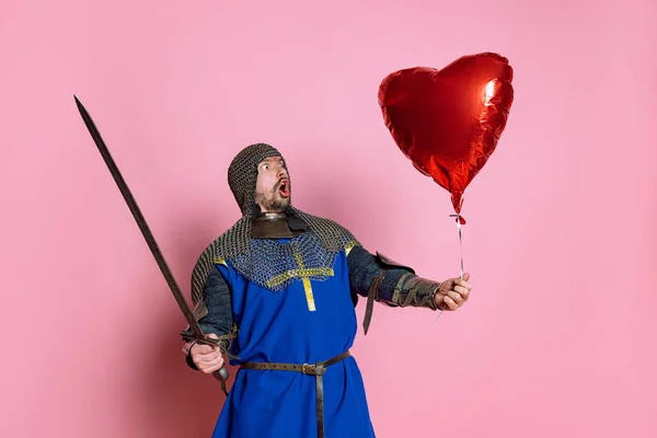Portret zszokowanego i podnieconego mężczyzny, średniowiecznego wojownika lub rycerza z czerwonym balonem w kształcie serca odizolowanego na różowym tle — Zdjęcie stockowe