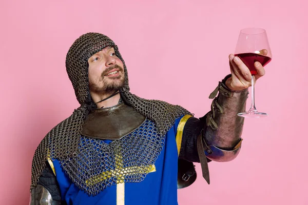 Pół-długi portret człowieka, średniowiecznego wojownika lub rycerza w ochronnej zbroi łańcuchowej podnoszącej szklankę winorośli odizolowanej na różowym tle studia — Zdjęcie stockowe