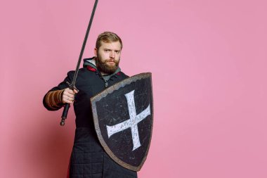 Genç cesur bir adamın portresi, orta çağ savaşçısı ya da kılıç ve koruyucu kalkanlı okçu pembe stüdyo arka planında izole edilmiş.