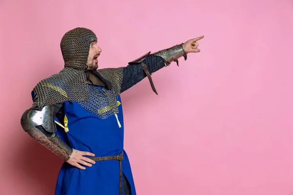 Retrato de vista lateral del hombre, guerrero medieval o caballero en armadura de cadena apuntando, dando instrucciones aisladas sobre fondo de estudio rosa —  Fotos de Stock