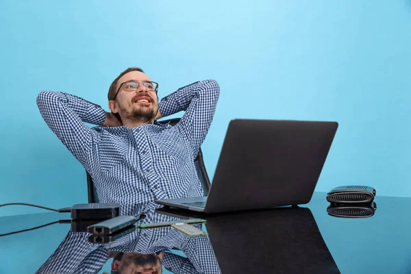 Портрет щасливого чоловіка, спеціаліста з комп'ютерної підтримки, програміста, що сидить перед ноутбуком ізольовано на синьому фоні — стокове фото