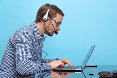 Ciddi bir adamın yan görünüş portresi, profesyonel bilişim programcısı, çağrı merkezi operatörü mavi arka planda laptopla çalışan.