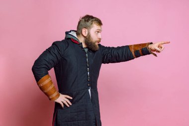 Ortaçağ okçusu kostümü giymiş genç sakallı bir adamın portresi pembe arka planda duygusal olarak izole edilmiş. Duygular konsepti