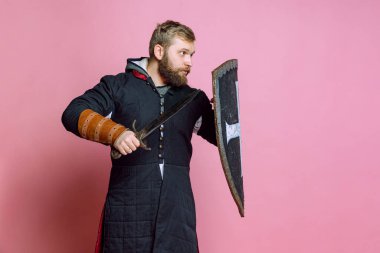 Genç cesur bir adamın portresi, orta çağ savaşçısı ya da kılıç ve koruyucu kalkanlı okçu pembe stüdyo arka planında izole edilmiş.