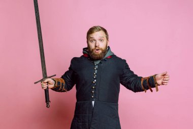 Şok olmuş genç bir adam, ortaçağ savaşçısı ya da kılıçlı bir okçu pembe stüdyo arka planında ağzı açık kameraya bakıyor. Dönem Karşılaştırması