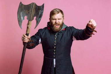 Ortaçağ savaşçısı suretinde genç sakallı bir adamın atölye fotoğrafı pembe arka planda izole edilmiş baltalı zırhlı okçuluk. Dönem Karşılaştırması