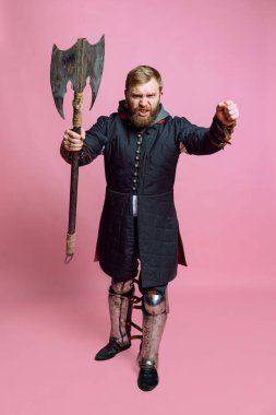 Ortaçağ savaşçısı suretinde genç sakallı bir adamın atölye fotoğrafı pembe arka planda izole edilmiş baltalı zırhlı okçuluk. Dönem Karşılaştırması