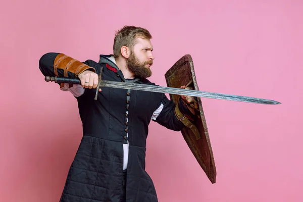 Портрет молодого храброго человека, средневекового воина или лучника с мечом и защитным щитом на фоне розовой студии — стоковое фото