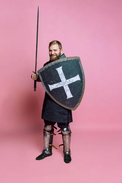 若い勇敢な男、中世の戦士や剣とピンクのスタジオの背景に隔離された保護シールドと射手の肖像画 — ストック写真